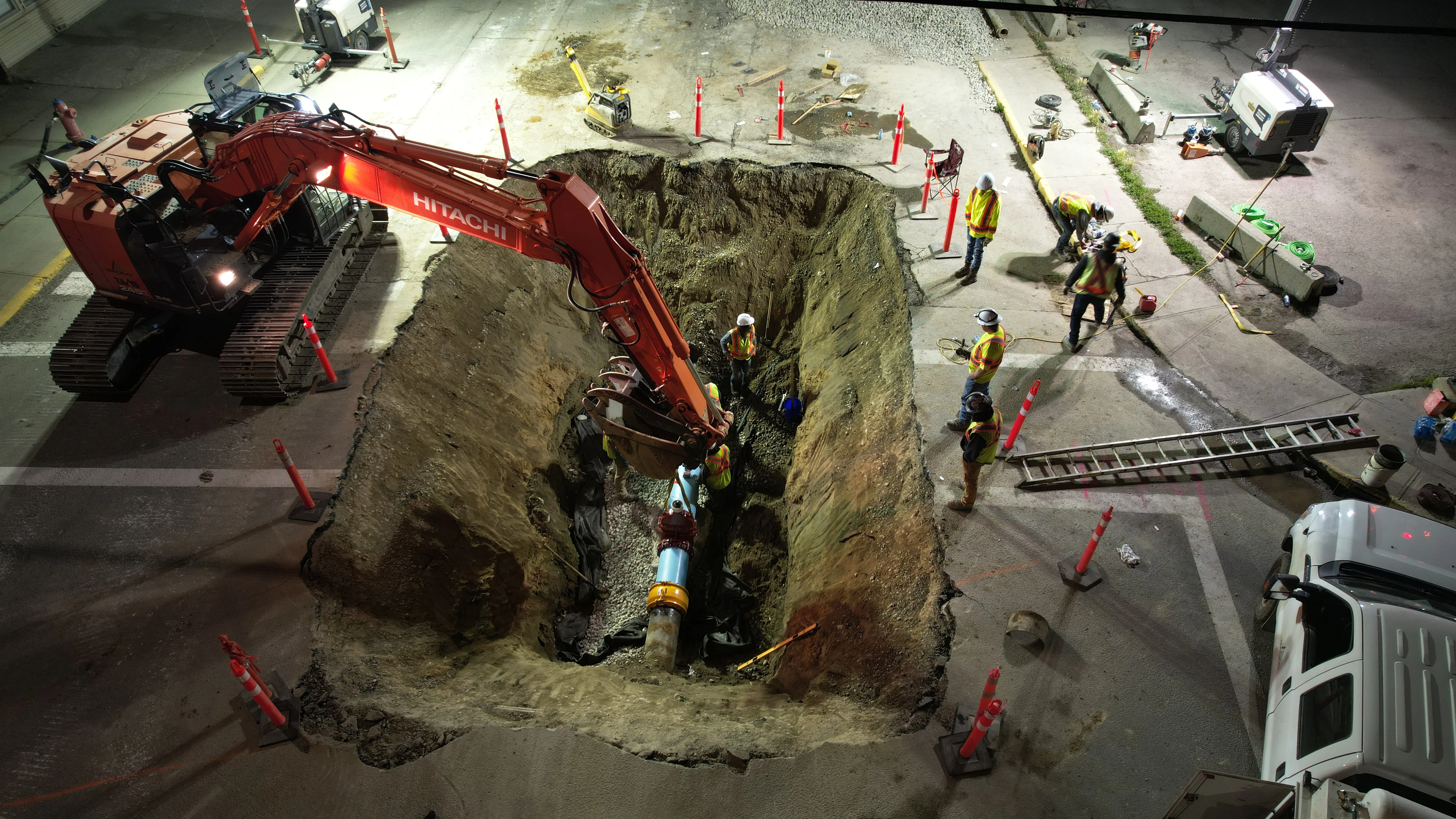 Crew installing a new watermain in a lit excavation during night work