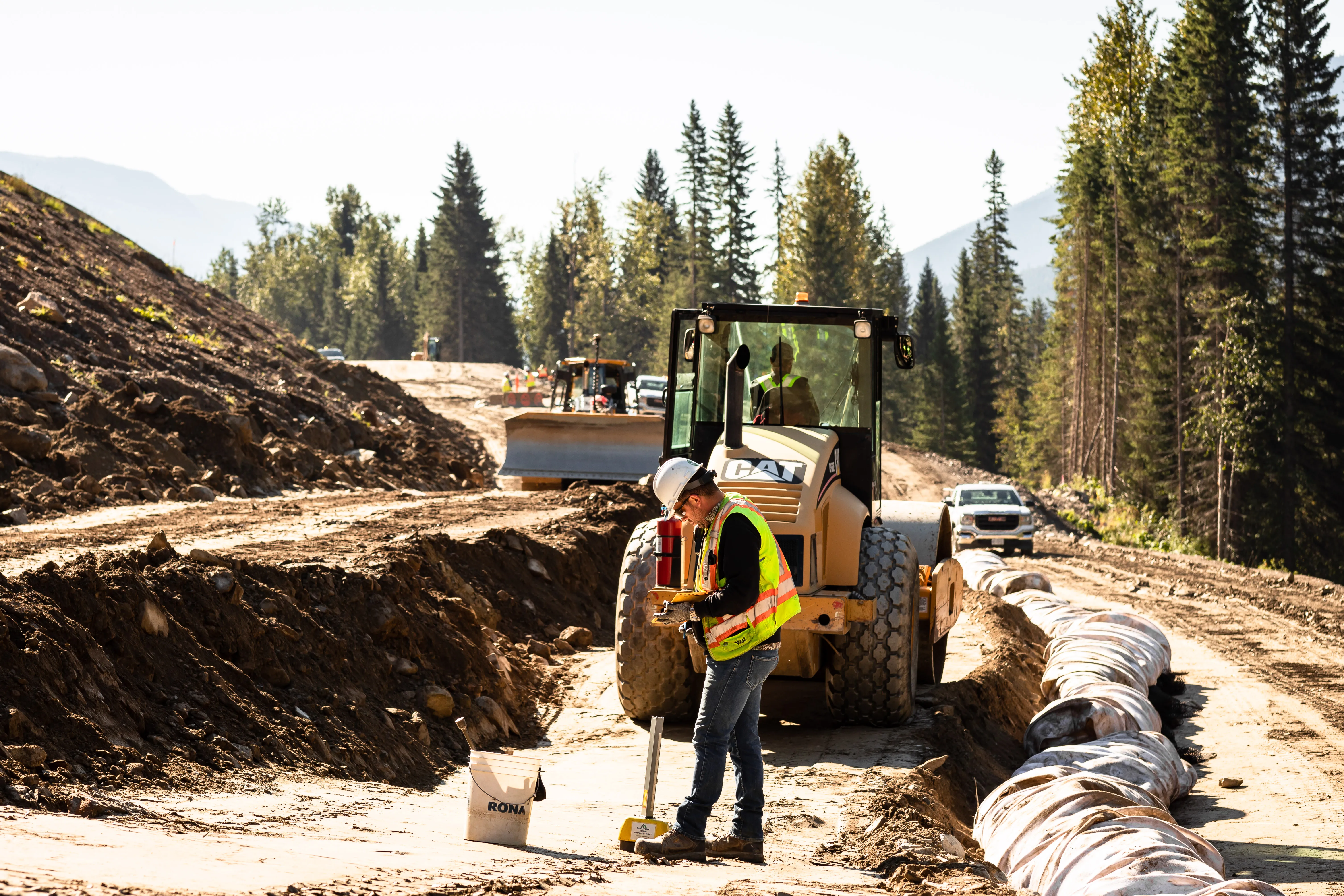 Compaction and grading crew working a new road corridor through forested terrain